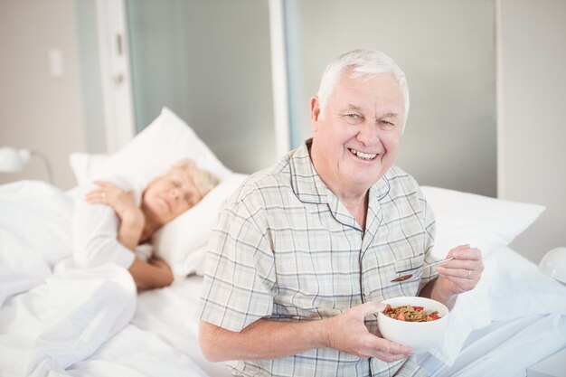 Hombre senior feliz comiendo ensalada por esposa dormida