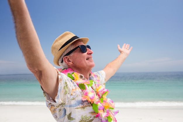 Hombre senior feliz con guirnalda de flores y disfrutando en la playa