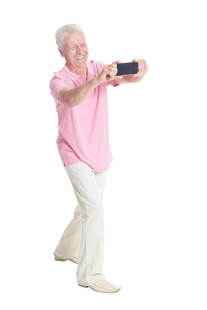 Hombre senior feliz con smartphone, tomando selfie sobre fondo blanco.