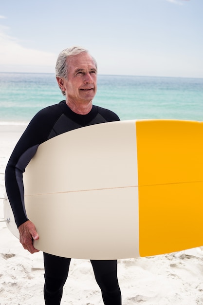 Hombre senior feliz en traje de neopreno con una tabla de surf