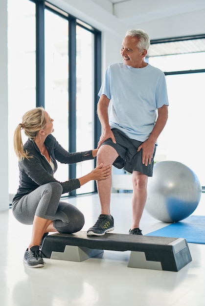 Hombre senior de fitness y fisioterapeuta con pierna para estiramiento, masaje y asistencia para el bienestar, paciente y mujer de rehabilitación con ayuda para el ejercicio de fisioterapia y apoyo para la recuperación.