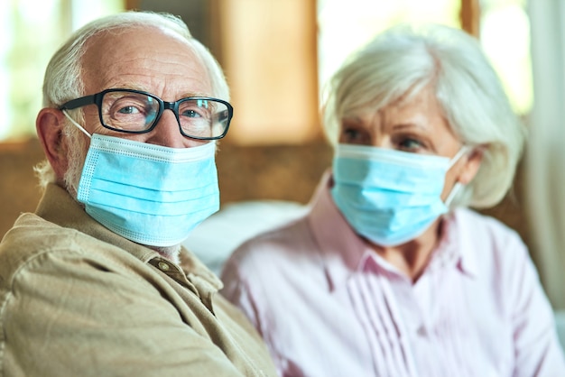 Hombre senior con gafas sentado junto a su esposa y usando máscaras