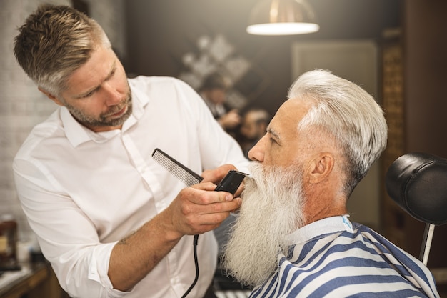 Hombre senior guapo obteniendo estilo y corte de barba en la barbería