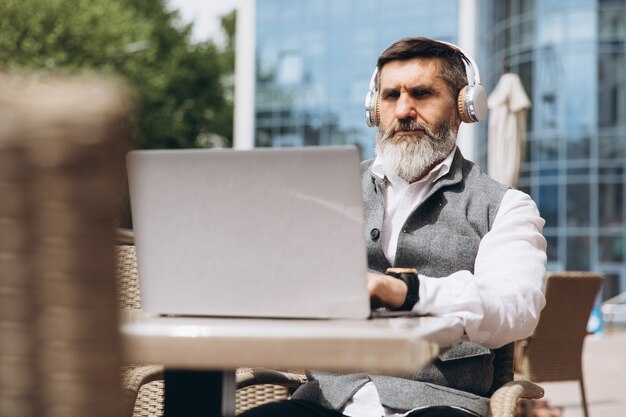 Hombre senior hombre elegante con barba gris pasa tiempo al aire libre en la computadora portátil