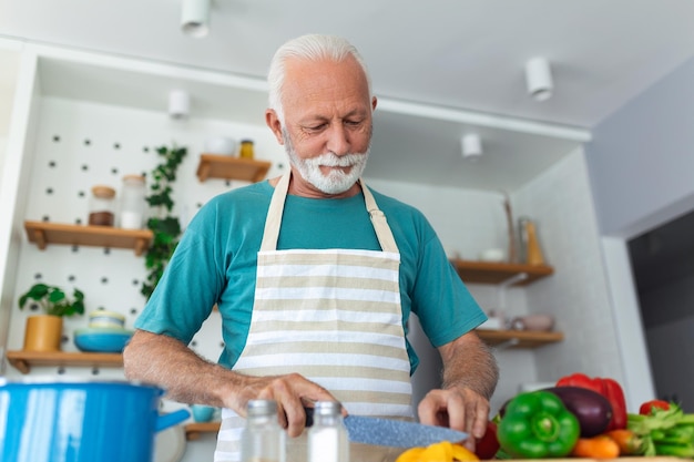 Hombre senior jubilado feliz cocinando en la cocina Concepto de personas aficionadas a la jubilación Retrato de un hombre senior sonriente cortando verduras