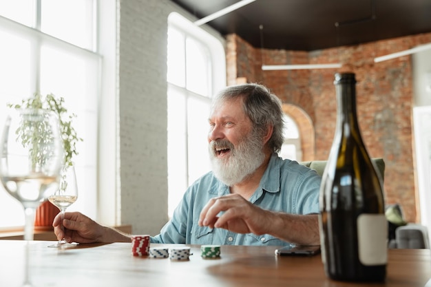 Hombre senior jugando a las cartas y bebiendo vino con amigos