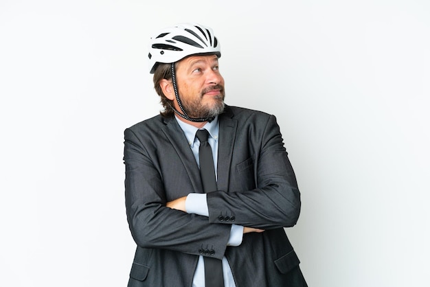 Hombre senior de negocios con un casco de bicicleta aislado sobre fondo blanco haciendo gesto de dudas mientras levanta los hombros