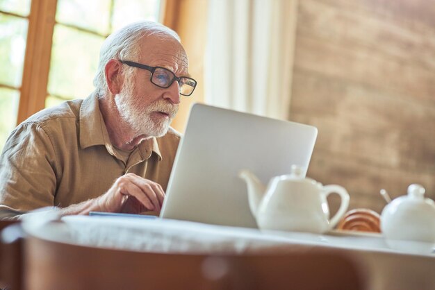 Hombre senior de pelo gris usando la computadora mientras escribe