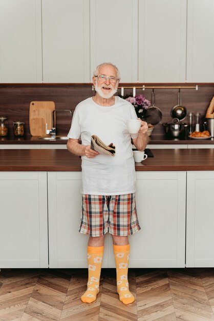 Hombre Senior relajándose en casa, leyendo el periódico y desayunando