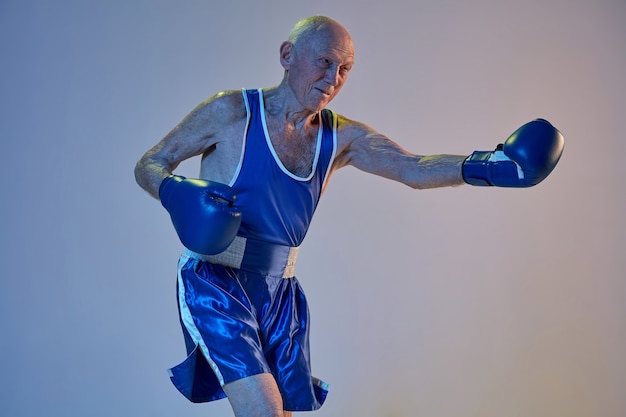 Hombre senior con ropa deportiva de boxeo aislado en la pared del estudio  degradado