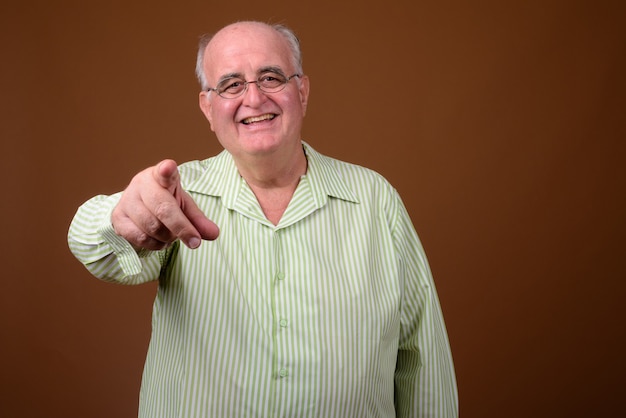 Foto hombre senior con sobrepeso con anteojos contra la pared marrón