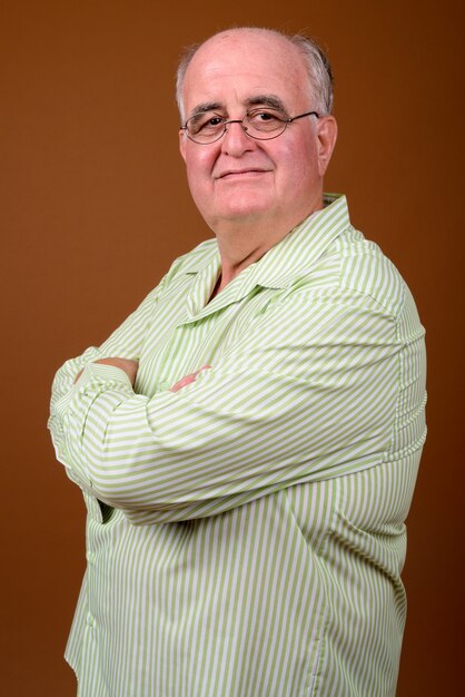 Foto hombre senior con sobrepeso con anteojos contra la pared marrón