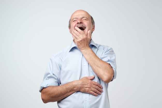 Hombre senior soñoliento bostezando después de un duro día de trabajo