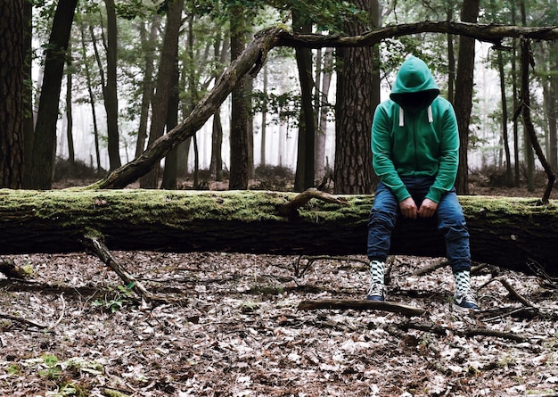 Foto hombre sentado en un árbol caído en el bosque