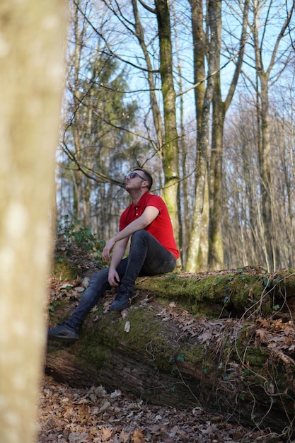 Foto hombre sentado en un árbol caído en el bosque