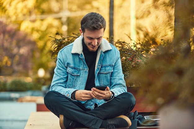 Un hombre sentado en un banco en el centro de la ciudad usando su teléfono inteligente y auriculares inalámbricos para una llamada