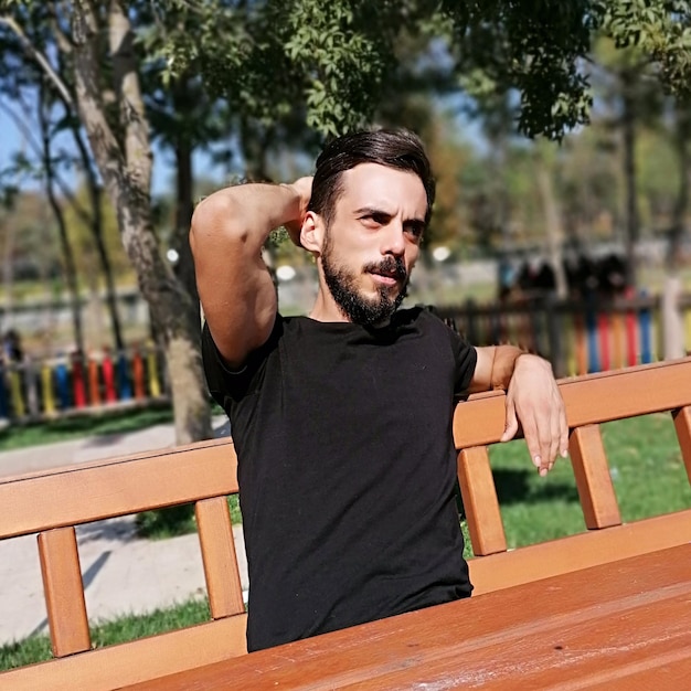 Foto hombre sentado en un banco contra un árbol en el parque