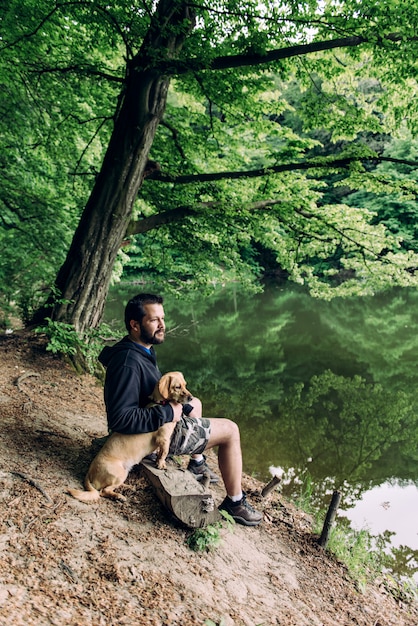 Hombre sentado en el banco con el perro junto al lago
