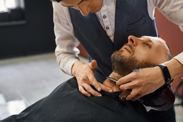 Hombre sentado en la barbería mientras el peluquero se afeita la barba