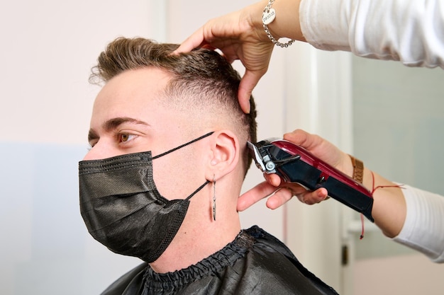 un hombre sentado en la barbería mientras el peluquero le peinaba el cabello con un cortapelos eléctrico