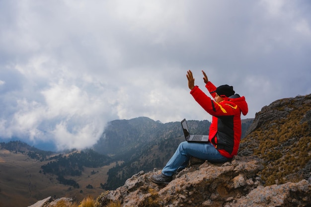 Hombre sentado en el borde del acantilado con vista panorámica a la montaña. Trabajo y viajes distantes, autónomo como concepto de estilo de vida