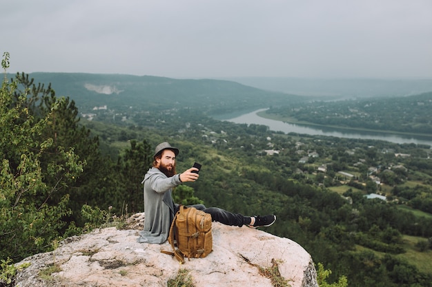 Hombre sentado en la cima de la montaña tomar selfie