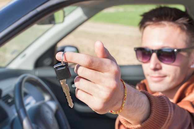 Hombre sentado dentro del coche y mostrando las llaves del coche nuevo