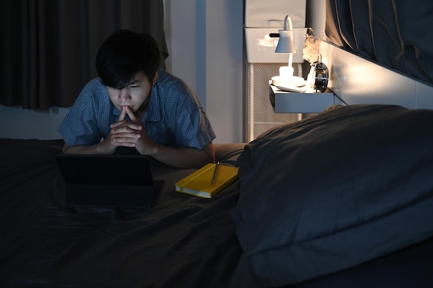 Hombre sentado en el dormitorio y usando una tableta de computadora a altas horas de la noche