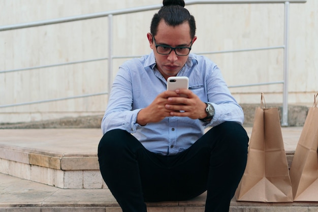 Hombre sentado en las escaleras con la bolsa de compras comprobando el teléfono celular