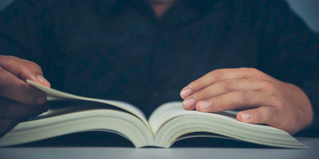 Hombre sentado en el escritorio leyendo un libro a altas horas de la noche Concepto de conocimiento y aprendizaje