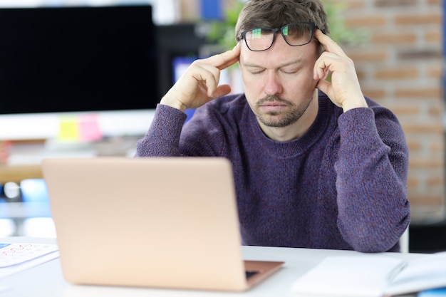 Hombre sentado frente a la computadora portátil y sosteniendo su cabeza. Concepto de cansancio en el trabajo