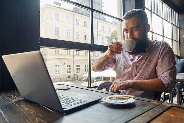 Hombre sentado frente a la computadora y tomando café