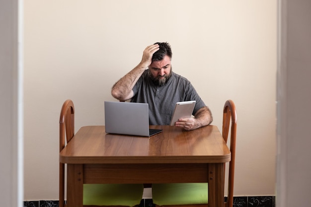 Hombre sentado frente a una mesa con una computadora portátil y una tableta con un problema