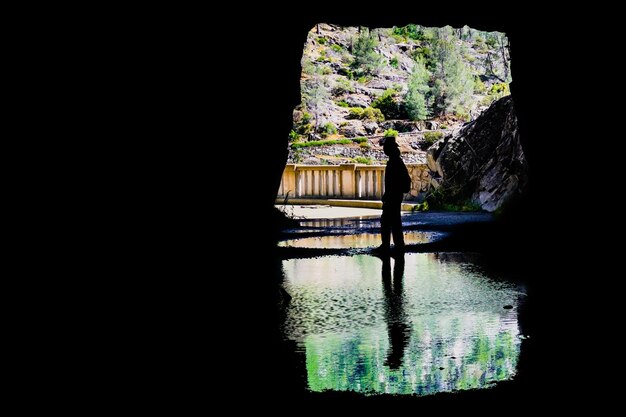 Hombre sentado frente a la salida de un túnel silueta reflejada en un estanque poco profundo Hetch Hetchy área del embalse Parque Nacional Yosemite Sierra Nevada California