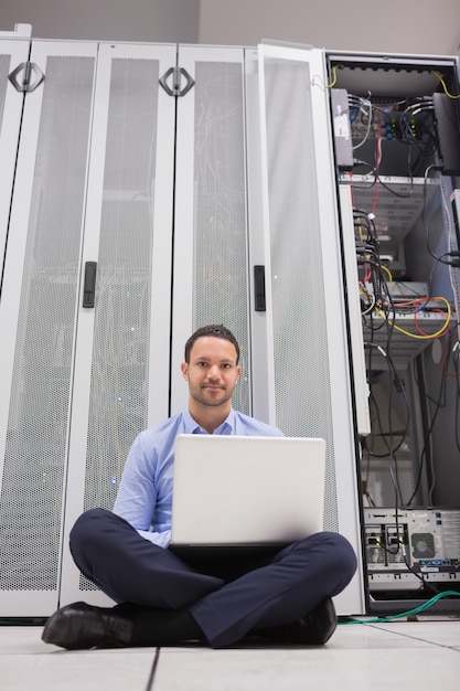 Foto hombre sentado frente a los servidores con su computadora portátil