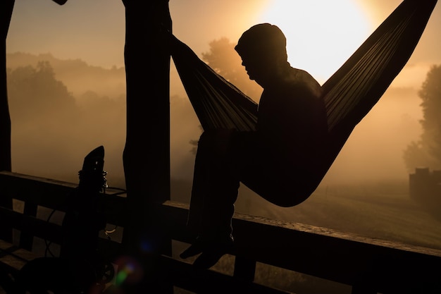 Foto hombre sentado en una hamaca contra el cielo durante la puesta de sol