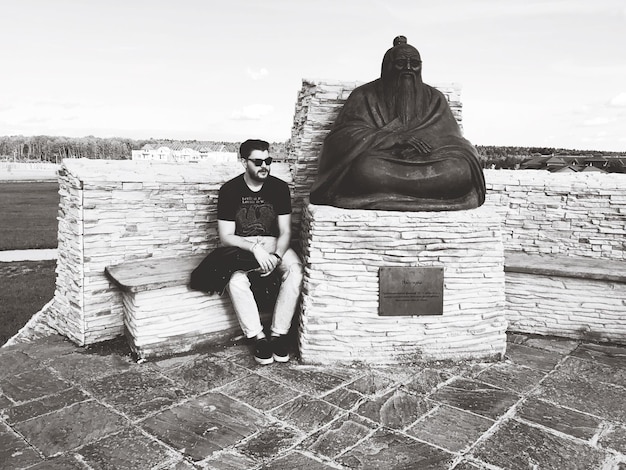 Foto hombre sentado junto a una estatua contra el cielo