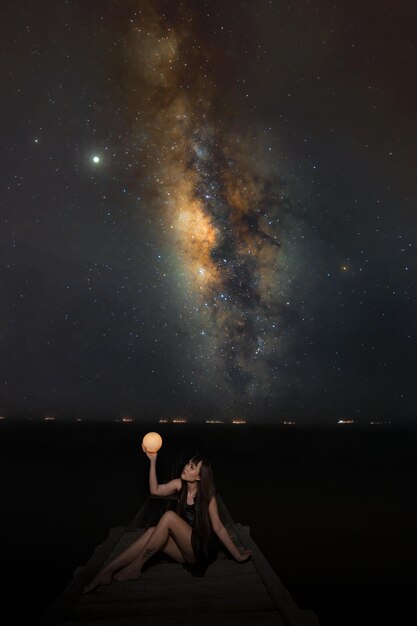 Foto hombre sentado junto a una roca contra el cielo por la noche