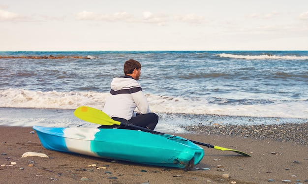 Hombre sentado en kayak en la playa del mar