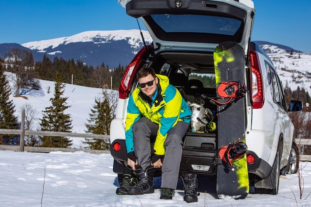 Hombre sentado en el maletero del coche cambiándose por snowboard