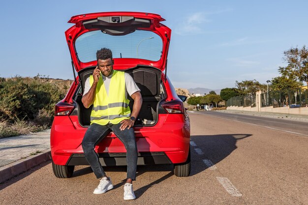 Hombre sentado en el maletero de un coche rojo