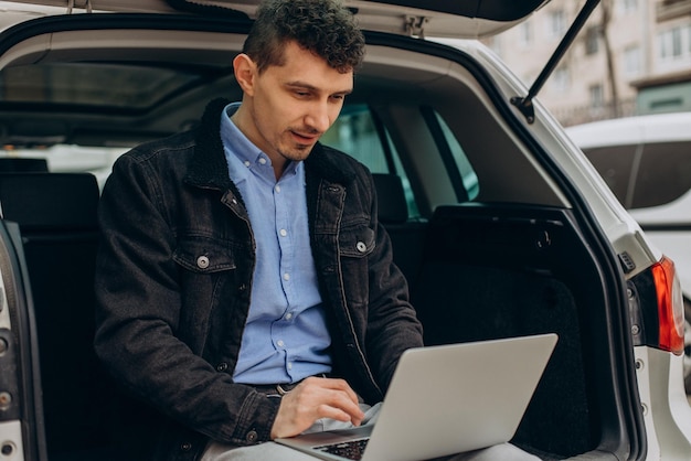 Hombre sentado en el maletero de su coche y trabajando en la computadora