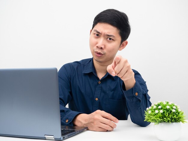 Un hombre sentado en la mesa con una laptop y te señala con el dedo una emoción seria