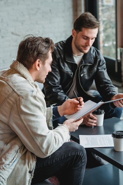 Foto un hombre está sentado en una mesa con un libro y un hombre está escribiendo en él