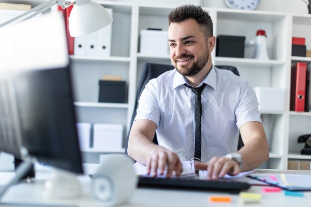 Foto un hombre está sentado en una mesa en la oficina, trabajando con documentos y una computadora.