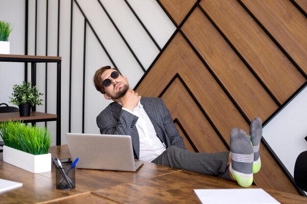 Foto un hombre está sentado en la oficina con una computadora portátil sus pies están en la mesa procrastinando