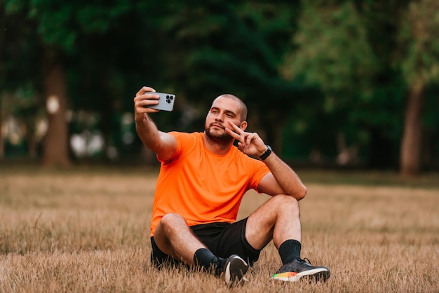 Un hombre sentado en el parque y haciéndose un selfie después de terminar su entrenamiento matutino