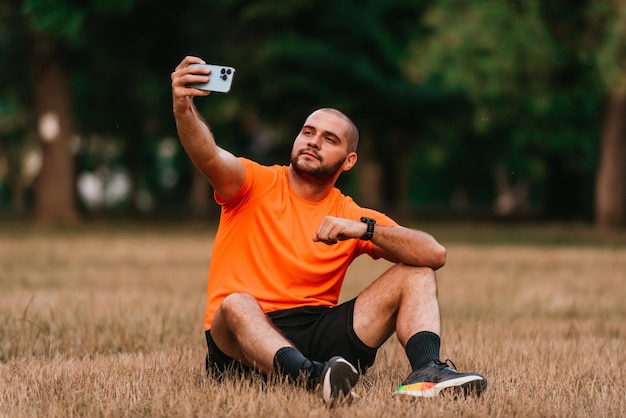 Un hombre sentado en el parque y haciéndose un selfie después de terminar su entrenamiento matutino