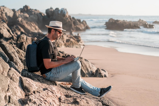 Hombre sentado en la playa con una computadora portátil solo haciendo teletrabajo o trabajo remoto