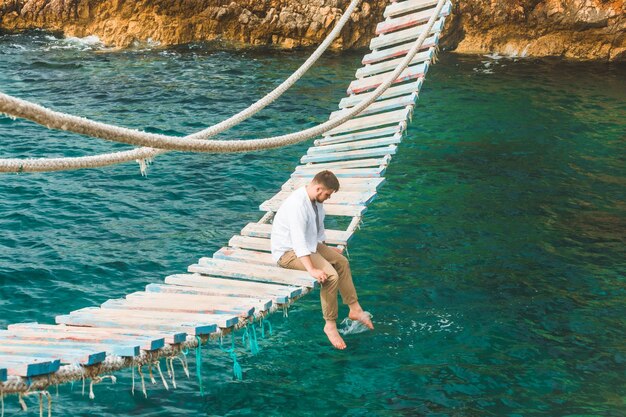 Hombre sentado en el puente colgante disfrutando de la vista al mar y la tranquilidad de la naturaleza